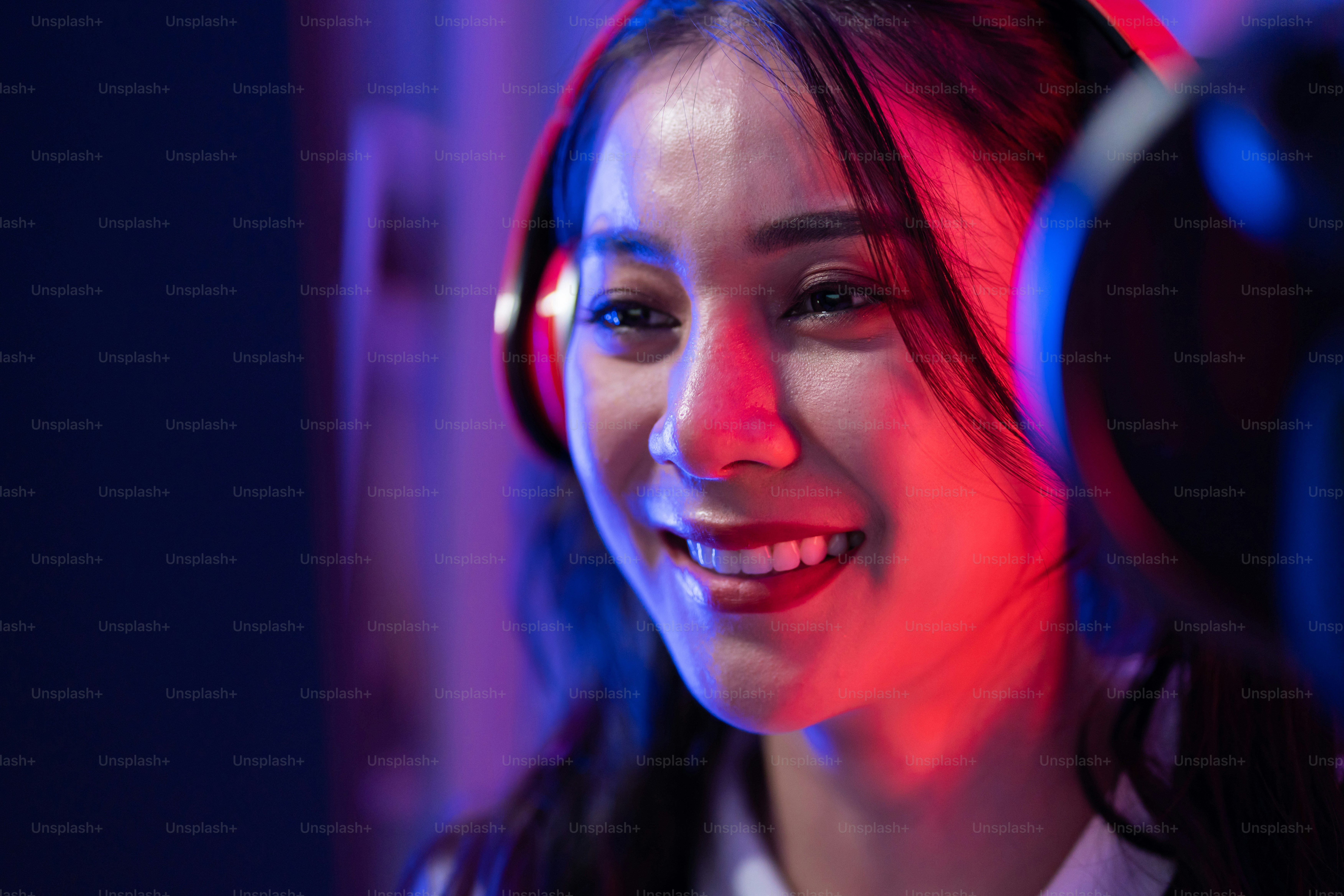 A smiling woman wearing red headphones in a room with blue and red lighting