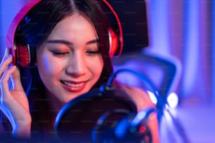 Asian attractive audio DJ woman speaks into microphone to broadcasting. Young beautiful female blogger influencer wearing headphones and recording morning news podcast show for radio at home studio.