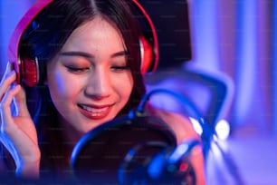 Asiática atractiva mujer DJ de audio habla por micrófono a la transmisión. Joven y hermosa bloguera influencer con auriculares y grabando un programa de podcast de noticias matutinas para la radio en el estudio de casa.