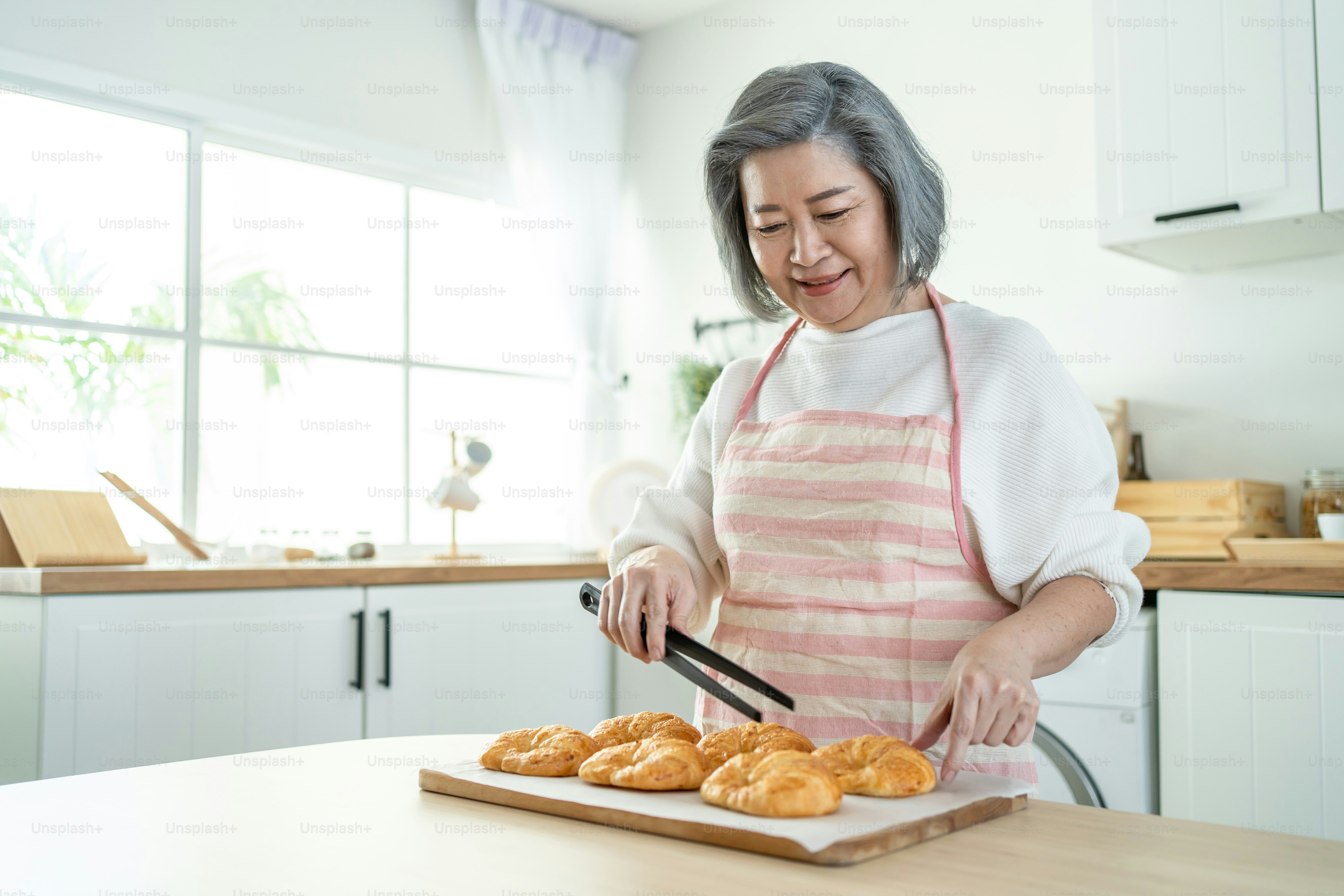 Portrait of Asian happy Senior elderly woman stand in kitchen at home. Attractive Older grandmother feeling happy and enjoy retirement life, cooking foods bake bakery and smiling in house.