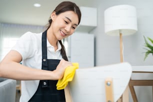 Asian cleaning service woman worker cleaning in living room at home. Beautiful girl housewife housekeeper cleaner feel happy and wiping messy dirty working table for housekeeping housework or chores.