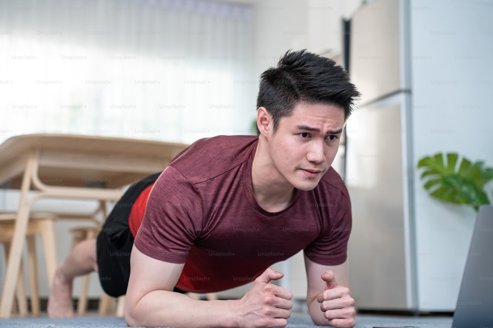 Asian handsome active young man doing push up on floor in living room. Attractive male in sport cloth spend leisure activity time to exercise and workout on holiday at home. Healthy lifestyle concept.