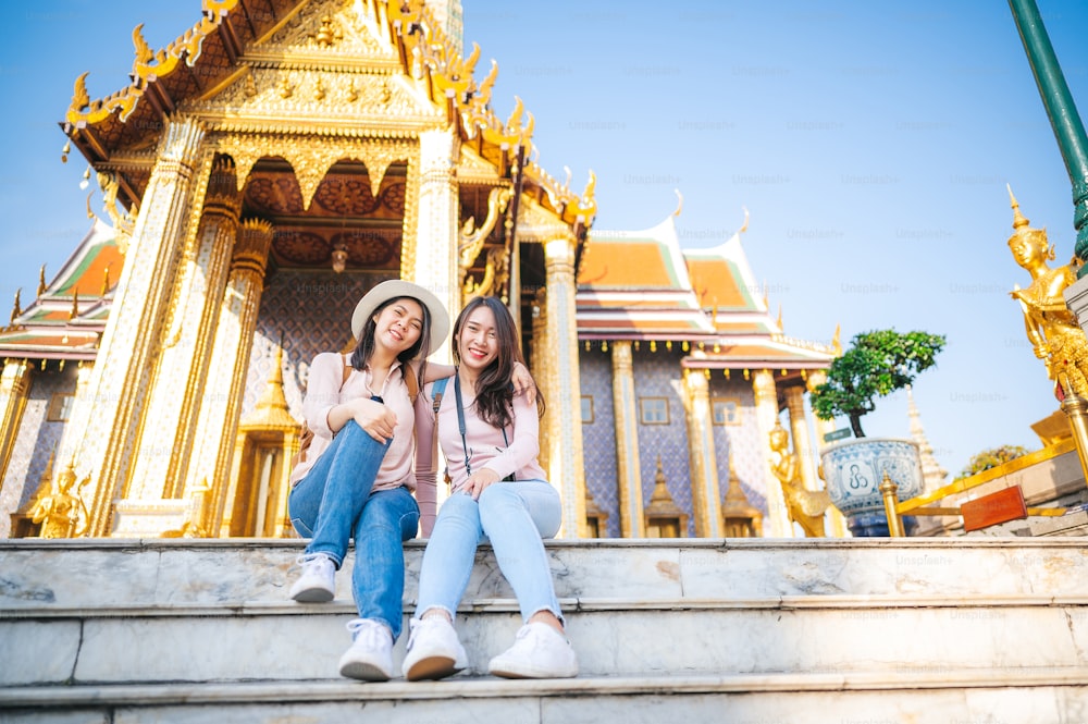 Tourist Asian women friends enjoy sightseeing while travel in temple of the emerald buddha, Wat Phra Kaew, popular tourist place in Bangkok, Thailand