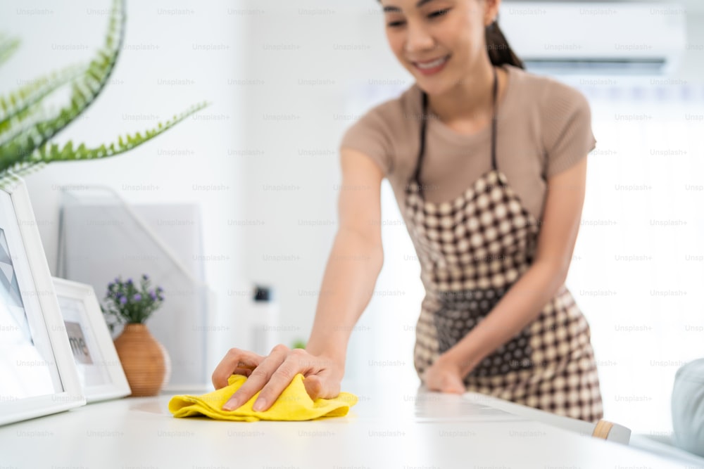 Asian cleaning service woman worker cleaning in living room at home. Beautiful girl housewife housekeeper cleaner feel happy and wiping messy dirty working table for housekeeping housework or chores.