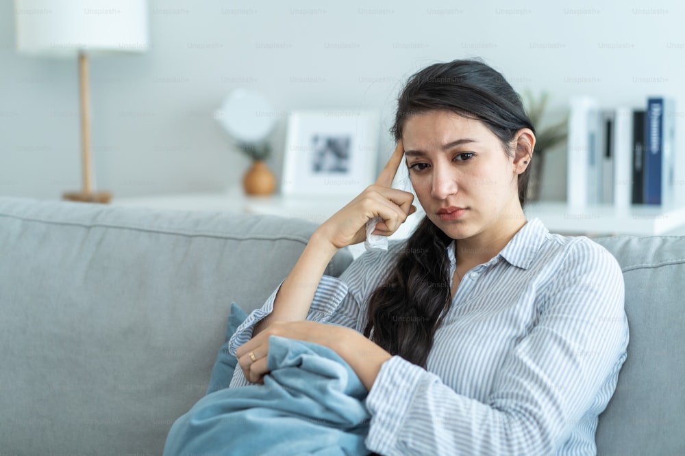 Asian beautiful unhappy woman sit on sofa feel frustrated and stressed. Attractive worried female having psychological problem feeling anxiety depression, upset and grief troubled for health at home.