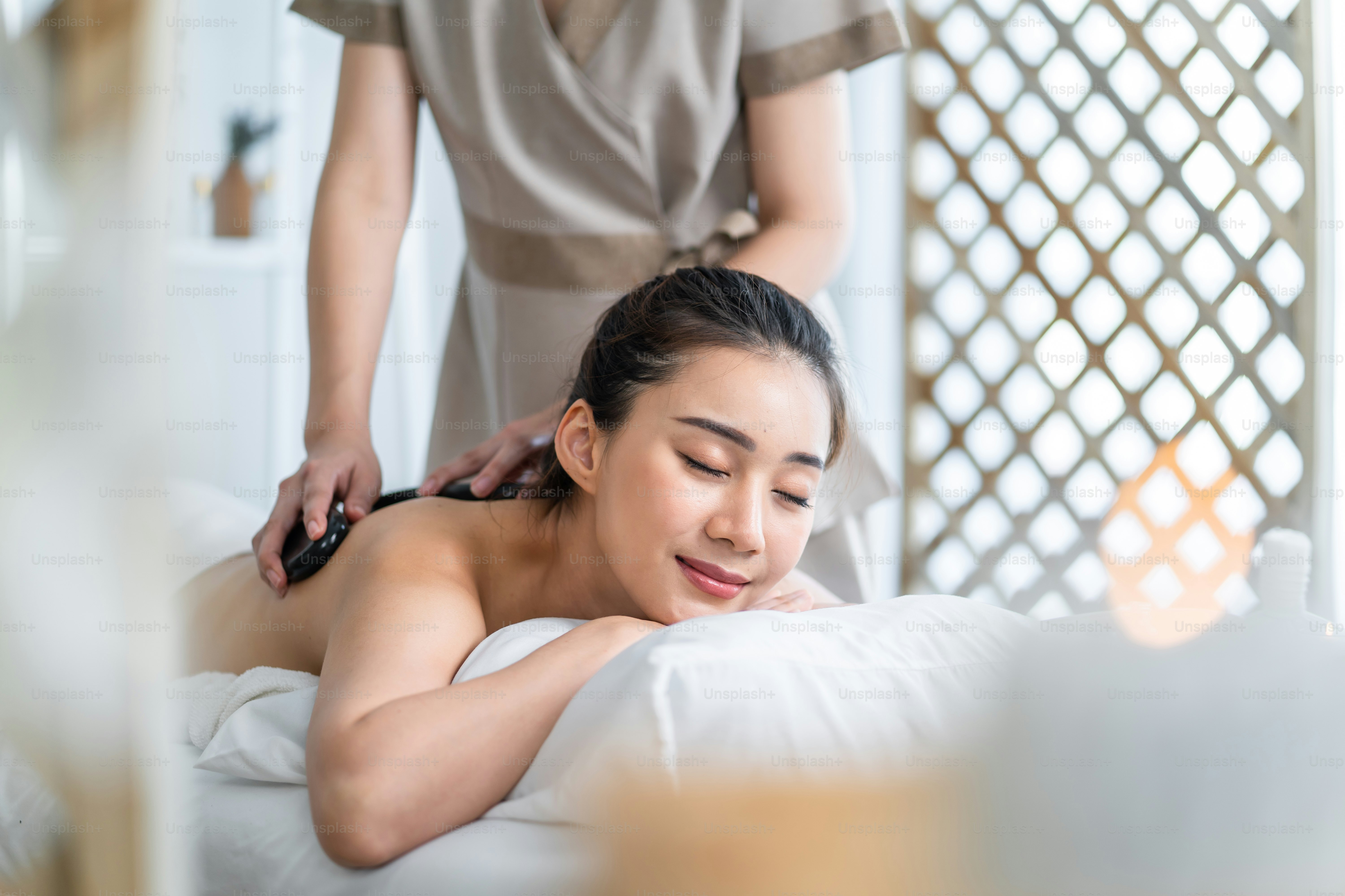 Asiatische junge Frau fühlt sich glücklich und entspannt sich bei der Rückenmassage mit Öl. Attraktives schönes Mädchen liegt auf dem Massagetisch und bekommt Physiotherapie von Masseurin für Haut- und Körperpflege im Spa-Schönheitssalon