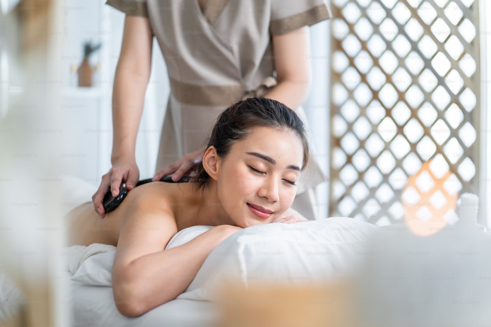 Asian young woman feeling happy and relax during back massage with oil. Attractive beautiful girl lying on massage table, getting physiotherapy from masseuse for skin and body care in spa beauty salon