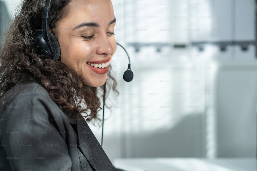 Latino beautiful business woman call center smile while work in office. Attractive young female employee worker in formal wear sit on table at workplace, use laptop computer talk to support customer.