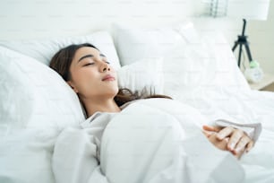 Asian beautiful comfort girl in pajamas get up from sleep in bedroom. Attractive young woman lying down on bed feel happy with cozy pillow and blanket enjoy early morning after wake up in room at home