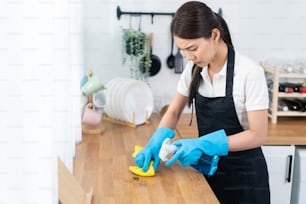 Asian young cleaning service woman worker clean kitchen table at home. Beautiful young girl housekeeper cleaner feel happy and wiping messy dirty cooking counter for housekeeping housework or chores.