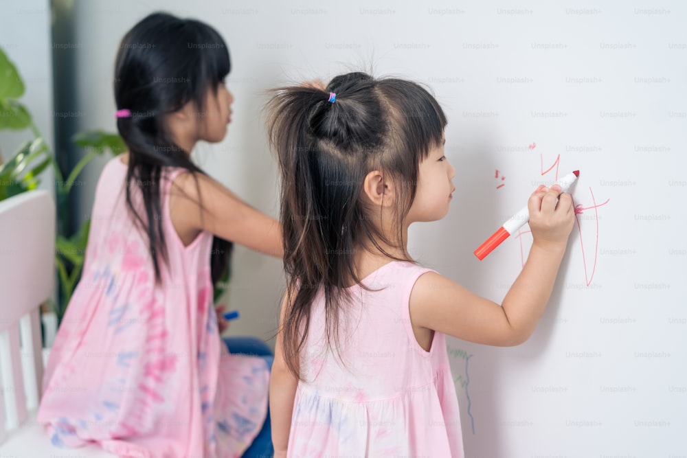 아시아 어린 형제 소녀가 거실의 흰 벽에 페인트를 칠하는 것을 즐긴다. 행복으로 예술 그림을 그리며 색칠하는 재미를 느끼는 작고 사랑스러운 아이들은 집에서 휴가를 보내는 창의력 활동을 즐깁니다.
