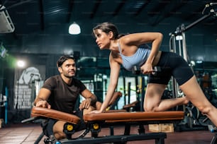 Caucasian Fitness trainer motivate young sportswoman to exercise in gym . Instructor coach teach Caucasian girl lift weight dumbbell for biceps to improve strength and maintain muscle at fitness club.