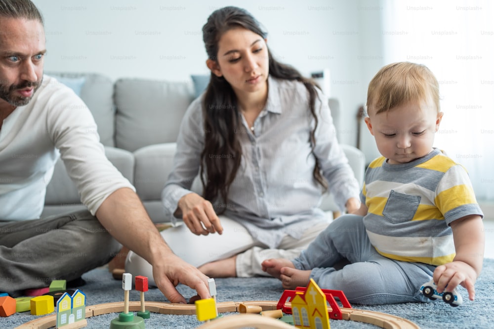 Caucasian happy loving parent play with baby toddler in living room. Attractive couple mother and father looking to young little infant son child's development. Activity relationship at home in house.