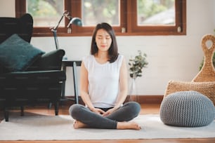 Felice donna asiatica sportiva attraente che pratica la meditazione a casa in soggiorno