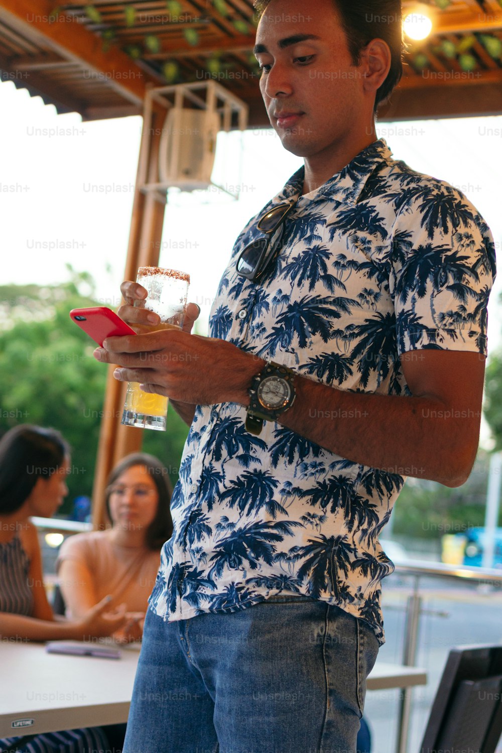 Homem latino com uma cerveja e um telefone em um bar, no fundo de um grupo de amigos em uma mesa.