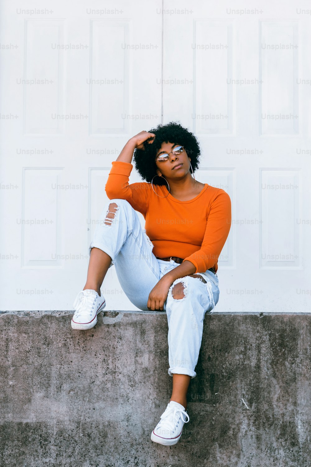Portrait de femme afro-américaine assise sur une porte blanche en plein air.