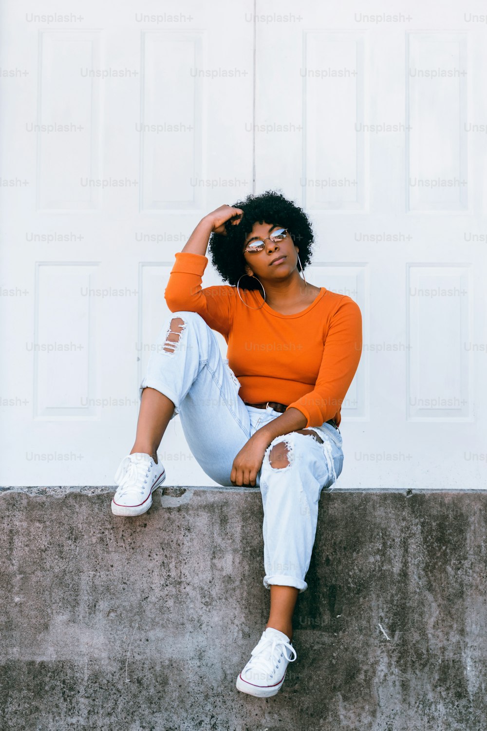 Retrato de la mujer afroamericana sentada en la puerta blanca al aire libre.