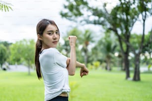 公園で屋外でヨガのトレーニングをしているアジアの若い美しいスポーツの女性。スポーツウェアを着た魅力的な痩せた女の子は、幸せを感じてリラックスし、公共の緑豊かな公園で健康管理のために体を伸ばす運動を楽しんでいます。