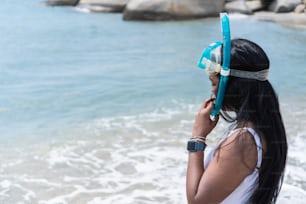 Afroamerikanische Frau im Badeanzug und wegschauend, während sie an einem sonnigen Sommertag eine Schutzbrille gegen das Meer trägt.