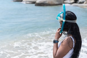 Afro-American woman in a bathing suit and looking away while wearing goggles against the sea on a sunny summer day.