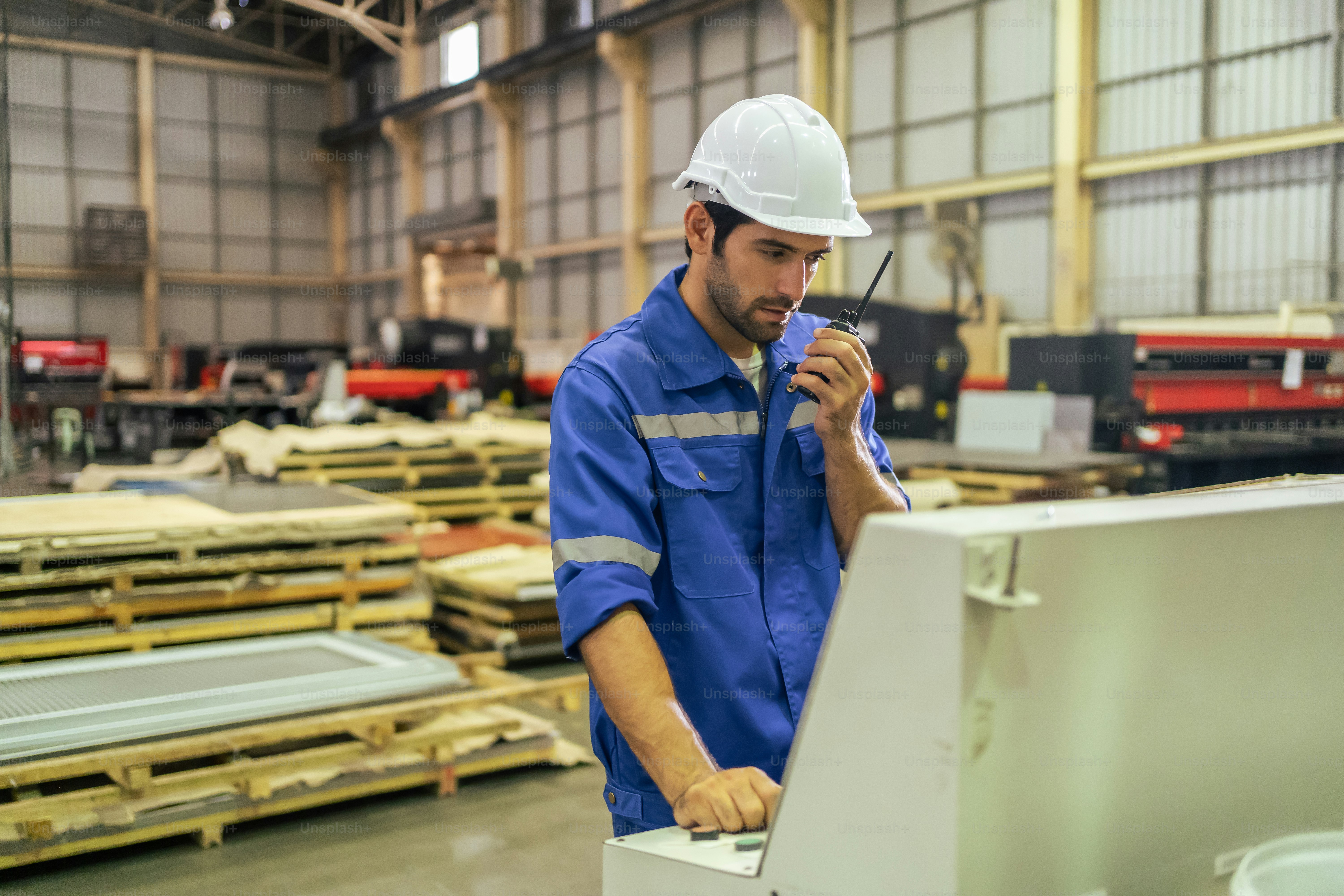 Trabajador industrial masculino guapo caucásico trabaja en la planta de fabricación. El ingeniero de la fábrica de la industria del hombre joven atractivo usa el casco y procesa los pedidos y el producto en la planta de fabricación con felicidad
