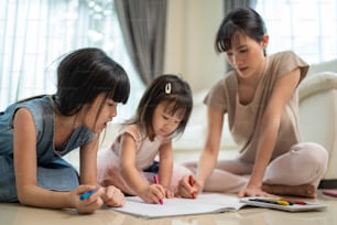 Asian loving parent spend time with small cute kid daughter enjoy activity at house. Little siblings girl artist having fun draw and color picture with mother on floor. Parenting relationship concept.