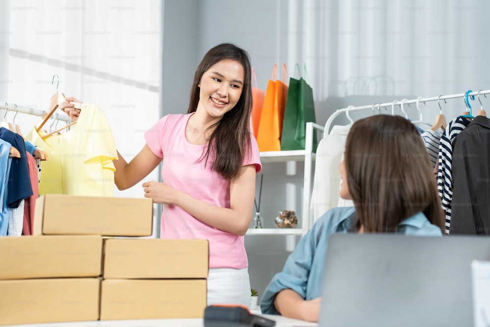 Asian woman friends couple packing clothes order into box for customer. Young  attractive business people work to preparing parcel boxes check ecommerce  shipping online retail to sell at office store. photo –