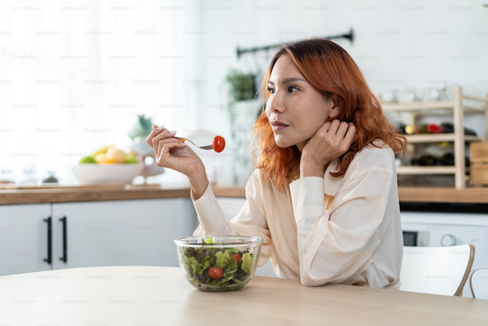 Asiatische junge glückliche attraktive Frau essen grünen Salat in der Küche zu Hause. Schönes Mädchen fühlen sich fröhlich und genießen es, Gemüse gesunde Lebensmittel zu essen Diät und Gewicht zu verlieren für die Gesundheitsfürsorge Wellness im Haus.