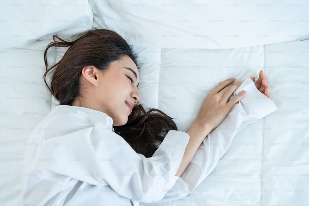Asian beautiful comfort sleepy girl in pajamas sleeping in bedroom. Attractive young woman lying down on bed feel happy with cozy pillow and blanket enjoy early morning after wake up in room at home.