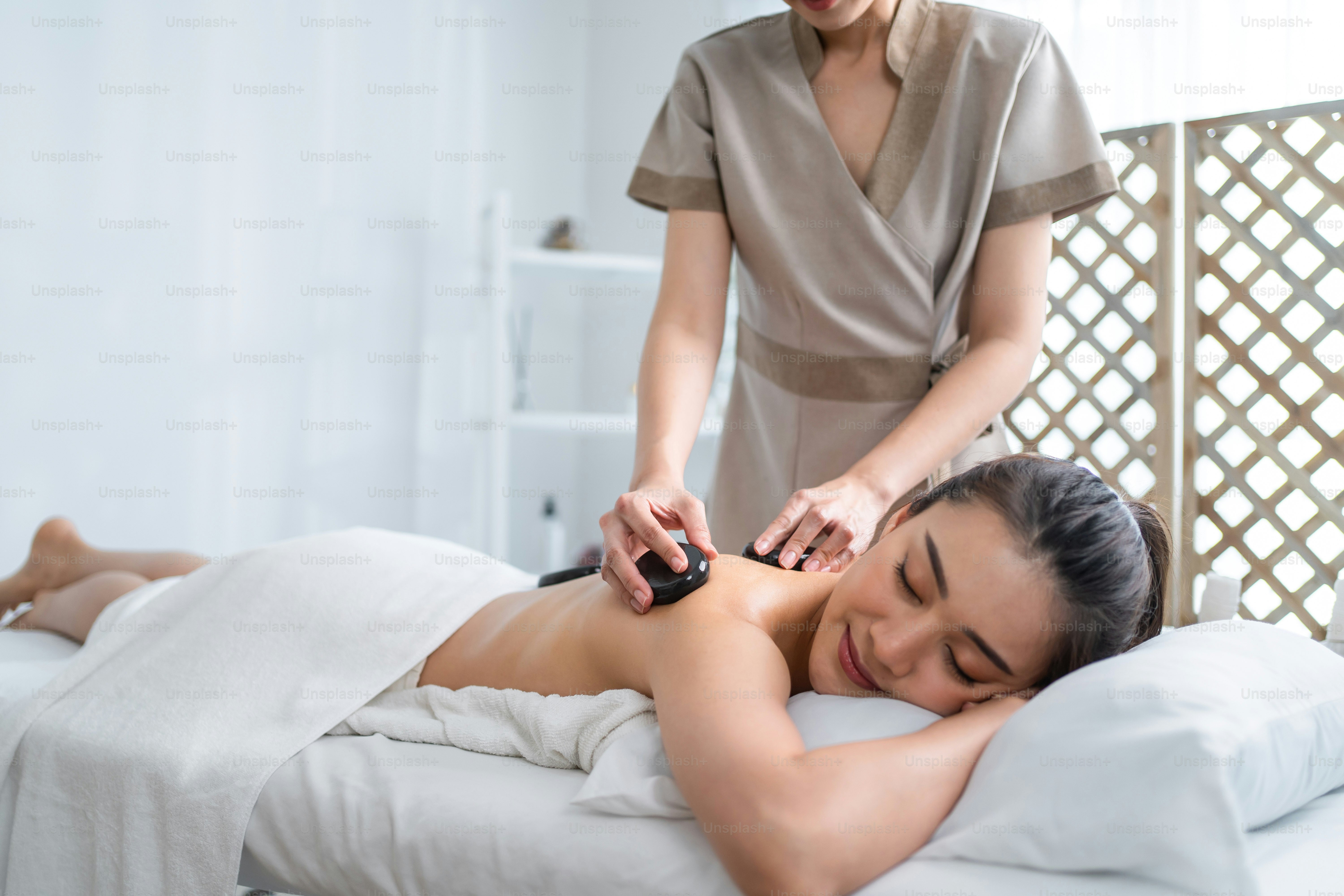 Wanita muda santai Asia mendapatkan terapi pijat kembali dengan batu panas. Gadis cantik yang menarik berbaring di meja pijat, mendapatkan fisioterapi dari tukang pijat untuk perawatan kulit dan tubuh di salon kecantikan spa