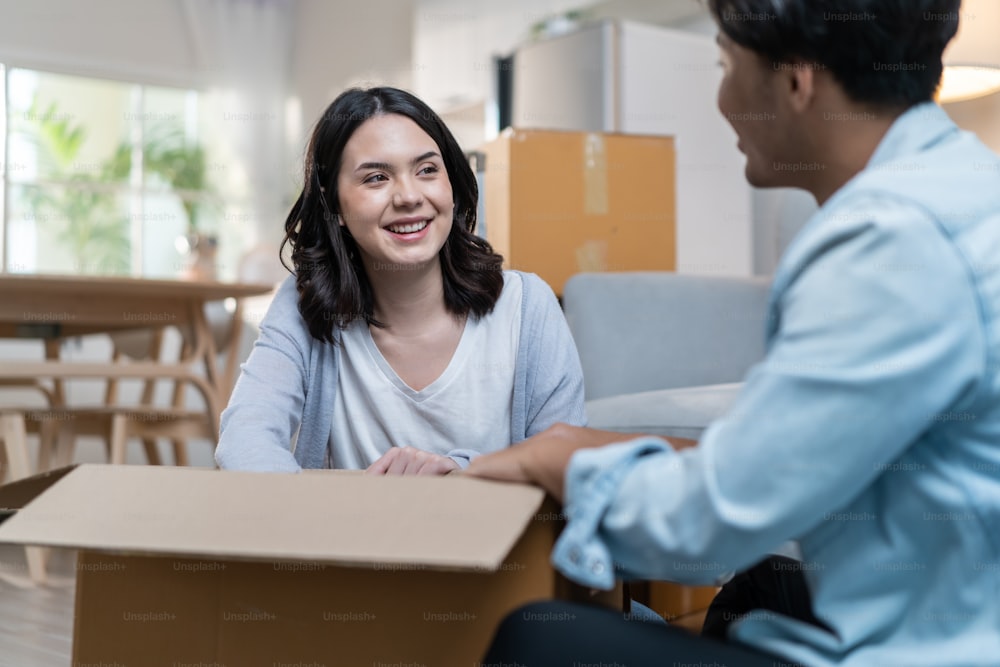 Asian young happy new marriage couple moving to new house together. Attractive romantic man and woman holding box parcel and suitcase with happiness and love. Family-Moving house relocation concept.