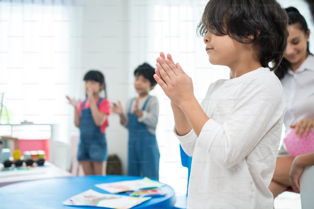 Group of Mixed race cute child standing clapping hands in classroom. Student young little kid boy applaud to answer questions in schoolroom enjoy to study with smiling, Feel glad and proud at school.