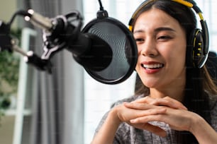 Asiatische attraktive Audio-DJ-Frau spricht in Mikrofon zum Rundfunk. Junge schöne weibliche Blogger-Influencerin, die Kopfhörer trägt und eine morgendliche Nachrichten-Podcast-Show für das Radio im Heimstudio aufnimmt.