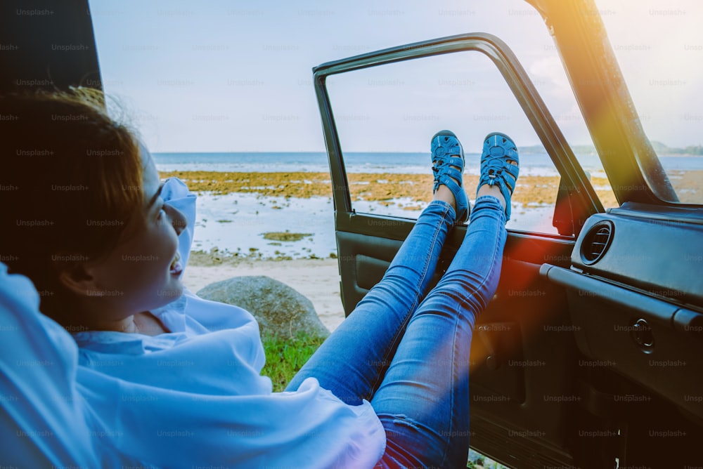 La mujer asiática viaja a la naturaleza. Viaja y relájate en la playa en verano. Sentado en el coche Feliz de ver el mar y la pierna fuera del coche.