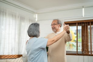 Asian happy Senior elderly Couple stay at home, spending leisure time in living room. Grandfather and grandmother enjoy retirement life and dancing together. Relationship and activity in house concept