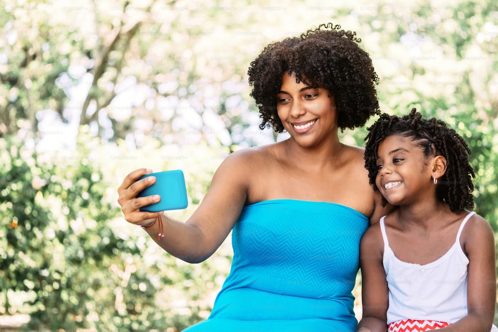 portrait of an afro american woman with a little girl smiling and joyful taking a selfie. technology concept.