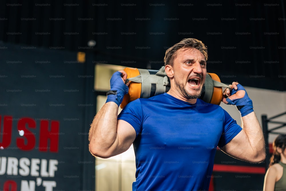 Kaukasischer Sportler hebt langsam Gewichtstasche oder Langhantel im Fitnessstudio. Attraktiver junger Athlet männlich trainiert Übung mit Kraftgeräten Werkzeug für die Gesundheitsversorgung und Erhaltung der Muskeln im Fitnessstudio.