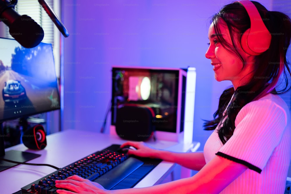 Asiática hermosa mujer jugadora de deportes juega videojuegos en línea en la computadora. La atractiva jugadora de juegos de la joven se siente feliz y disfruta de la transmisión de la tecnología en vivo mientras juega el torneo cibernético en casa