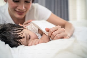 Asian loving beautiful mother take care asleep young comfortable kid. Caring parent mom put blanket on sleeping little small  girl daughter on bed in dark bedroom at night. Parenting activity at home.
