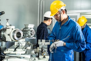 Asian mechanical workers working on milling machine. The technicians wearing protective glasses and helmet when operating the machine for safety precaution. The man working carefully prevent dangerous