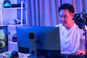El atractivo jugador masculino asiático de Esport juega un videojuego en línea en la computadora. El jugador de juegos de hombre guapo se siente feliz y emocionado, disfruta de la transmisión en vivo de la tecnología mientras juega un torneo cibernético en casa