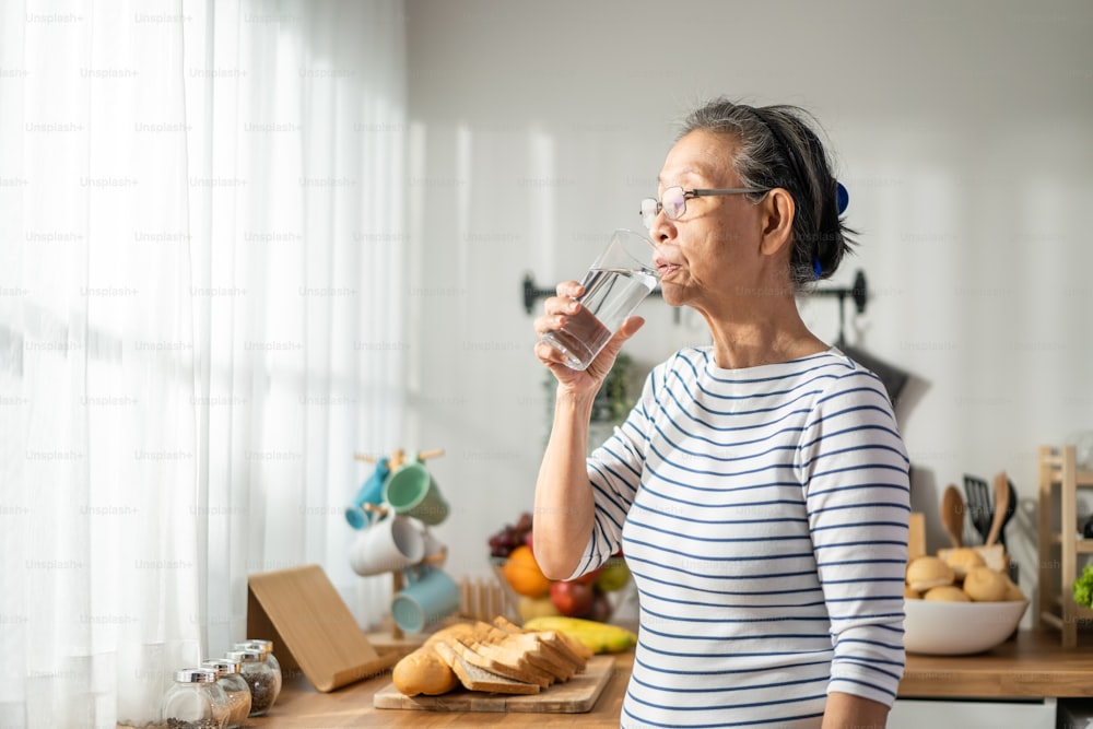 Femme mûre asiatique senior buvant un verre de lait dans la cuisine à la maison. Jolie grand-mère âgée tenant et sirotant une tasse de lait après s’être réveillée le matin pour des soins de santé à la maison.