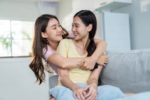 Asian beautiful lesbian women couple combing girlfriends hair in house. Attractive two female gay friend sit on sofa in living room, feel happy for beauty cosmetic together.