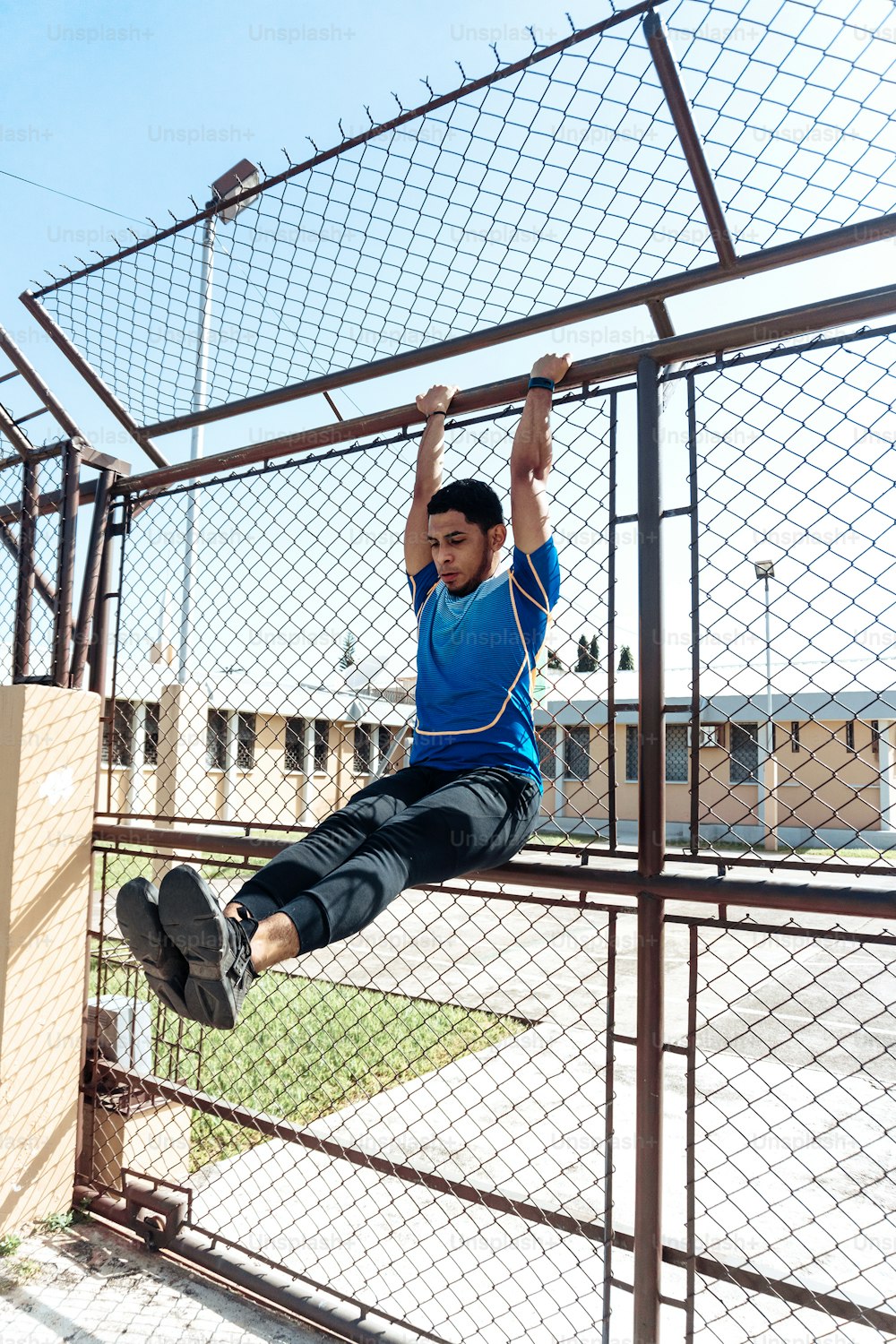 Young hispanic male exercising abs hanging on a grid fence