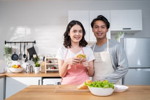 Portrait of Asian young new marriage couple cooking in kitchen at home. Happy family, Attractive lovely man and woman enjoy cooking healthy foods for breakfast in house and looking at camera together.