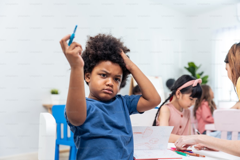 Portrait of Stressed African black child boy sitting in classroom. Depressed student little kid young boy feeling tired and worry while study art and drawing in schoolroom and look at camera at school