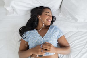 Young black woman in her bed listening to music with headphones at home inside her apartment. Feel good concept, happy. High quality photo.