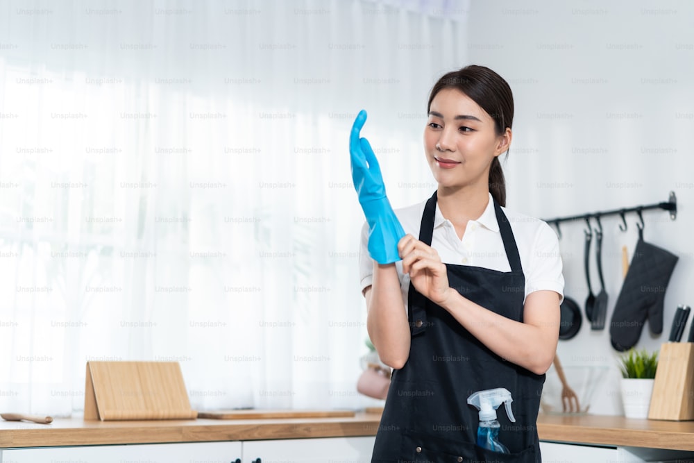 Ritratto di giovane donna asiatica di servizio di pulizia che lavora in casa. Bella donna casalinga donna pulitrice che indossa guanti protettivi e sorriso, pronta per fare le faccende domestiche o le faccende domestiche.