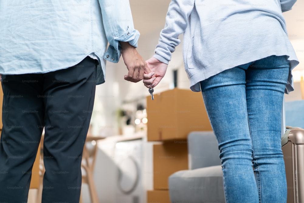 Close up hands of new marriage couple holding new house key together. Young attractive romantic man and woman holding suitcase moving to new home with happiness. Family-Moving house relocation concept