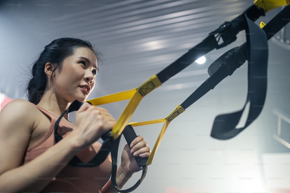Asian active athlete girl straight out her arms to hold rope anchored to a steel beam in stadium. Sportswoman Lifting up and down to maintain muscle, build strength, flexibility at fitness club or gym